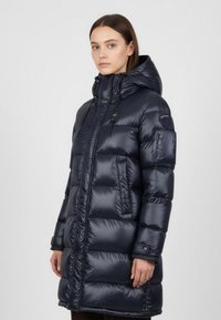 Námořnický pufový kabát s kapucí, s lesklým povrchem, prošívanými částmi a předním zipem. Obsahuje náprsní kapsu a nastavitelné šňůrky.