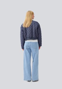 Veste cropped matelassée navy avec des poignets côtelés, associée à un jean large bleu clair. Coutures visibles et deux poches arrière sur le jean.