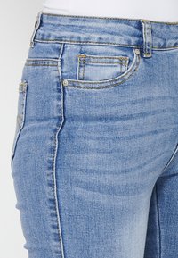 Light blue denim jeans featuring a slim fit, five-pocket design, subtle fading, and contrasting yellow stitching along the seams.