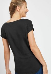 Svart kortärmad t-shirt med uppvikta ärmar, av bomullsmaterial, avslappnad passform, rund halsringning och mjuk textur.