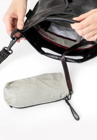 Borsa a tracolla in pelle nera con chiusura a zip e cuciture rosse. Include una piccola borsa di stoffa a righe posizionata accanto.