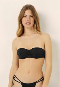 Svart bandeaukini�överdel med rynkad tygdesign och mjuk textur; i kombination med matchande bikinitrosor med justerbara sidoknyten.