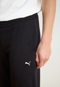 Sorte joggerbukser med en blød tekstur, der har en elastisk talje og et lille hvidt Puma-logo på venstre side.
