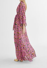 Lång, rosa klänning med djurmönster i gult, grönt och svart. Har breda ärmar och en knytning i midjan, gjord av lätt, genomskinlig tyg.