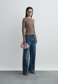 Striped ribbed long-sleeve top in brown and white, paired with loose-fitting blue jeans. Holds a pink textured clutch bag. Simple sandals complete the look.