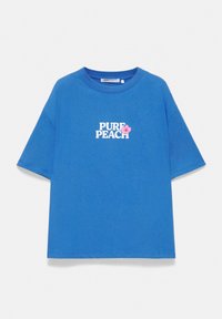 T-shirt bleu à manches courtes avec le texte « PURE PEACH » en blanc et un petit motif de fleur rose sur la poitrine, présenté sur fond blanc.