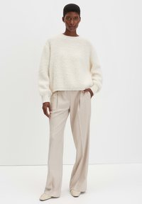 Romige gebreide trui met lange mouwen, gecombineerd met beige wijde broek en lichtgekleurde instap schoenen. Luxe, zachte stoffen.