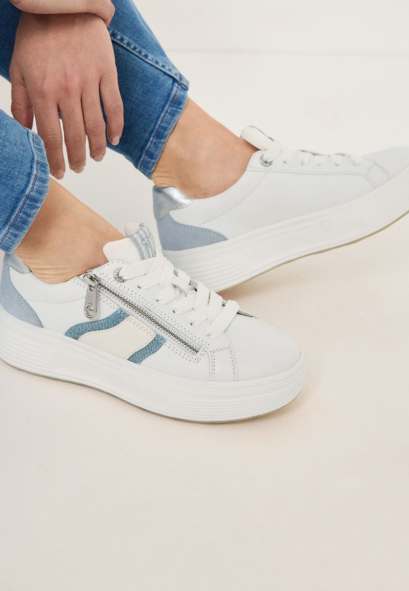 Sneakers bianchi con dettagli in denim, tacco argento e zip laterale. Presentano punta rotonda, suola piatta e design con lacci. Jeans blu visibili.