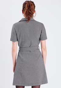 Robe à motifs noir et blanc avec manches courtes, col, taille cintrée et jupe évasée. Comprend une ceinture à la taille.