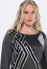 Donkergrijze top met geometrische zilveren patronen en de tekst "MODERN VIEW", gemaakt van een soepele stof met een ontspannen halslijn en lange mouwen.