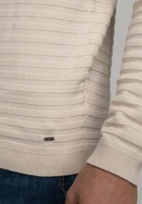 Beige gestreepte trui met een textuurafwerking, voorzien van een geribbelde zoom en manchetten. Opvallend klein metallic logo detail nabij de onderkant.