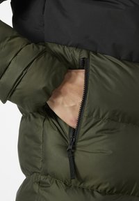 Chaqueta acolchada verde con una sección superior negra. Incluye un bolsillo lateral con cremallera negra y un acabado de tela texturizada.