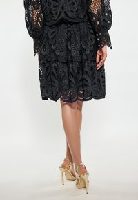 Vestito di pizzo nero con intricati motivi floreali, design a strati e orlo scallop. Abbinato a sandali con tacco alto dorati.