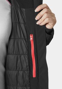 Czarna kurtka z pikowanym wzorem, jasnoróżowym zamkiem błyskawicznym i dopasowanym krojem. Zamek jest wyraźnie widoczny z boku.