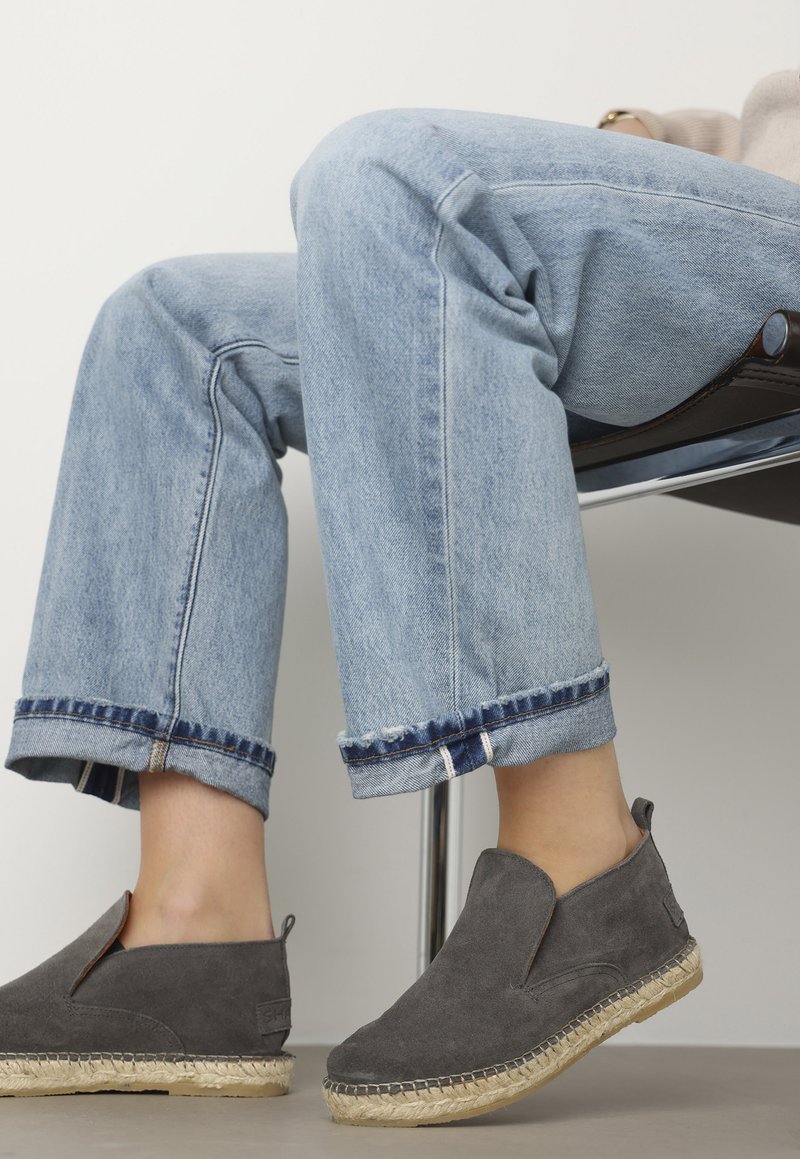 Scarpe slip-on grigie in suede con suola in juta, abbinate a jeans croppati azzurri chiari con orlo sfilacciato e accenti blu scuro.