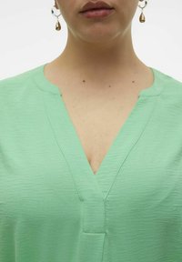 Mintgrøn v-hals bluse med en tekstureret overflade, der har subtil sømdetalje og en afslappet pasform. Tilføjer en frisk farve til hverdagstøj.