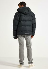 Doudoune noire avec capuche, présentant un design matelassé, des accents réfléchissants et une texture lisse. Associée à un jean gris et des baskets.