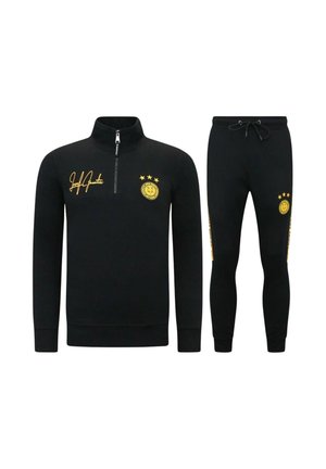 Zwarte sportpak met longsleeve half-ritstop en broek met trekkoord, beide met geel embleem en kenmerkende details op borst en dij.