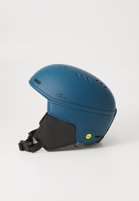 Modrá lyžiarska prilba s hladkým matným povrchom. Má viacero ventilačných otvorov, čierny remienok na brade a bezpečnostnú nálepku MIPS.