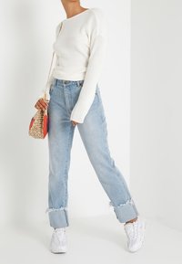 Valkoinen ribattu pitkähihaisuus neule, vaaleansiniset kulutetut suorat housut frayed-kunnolla, valkoiset lenkkarit ja kudottu käsilaukku.