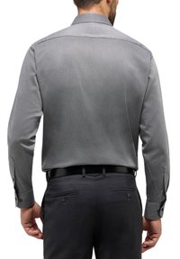 Graues Hemd mit Knöpfen, das ein dezentes Muster aufweist, lange Ärmel und Manschetten hat. Kombiniert mit dunklen Anzughosen, die über Gesäßtaschen und Knöpfe verfügen.