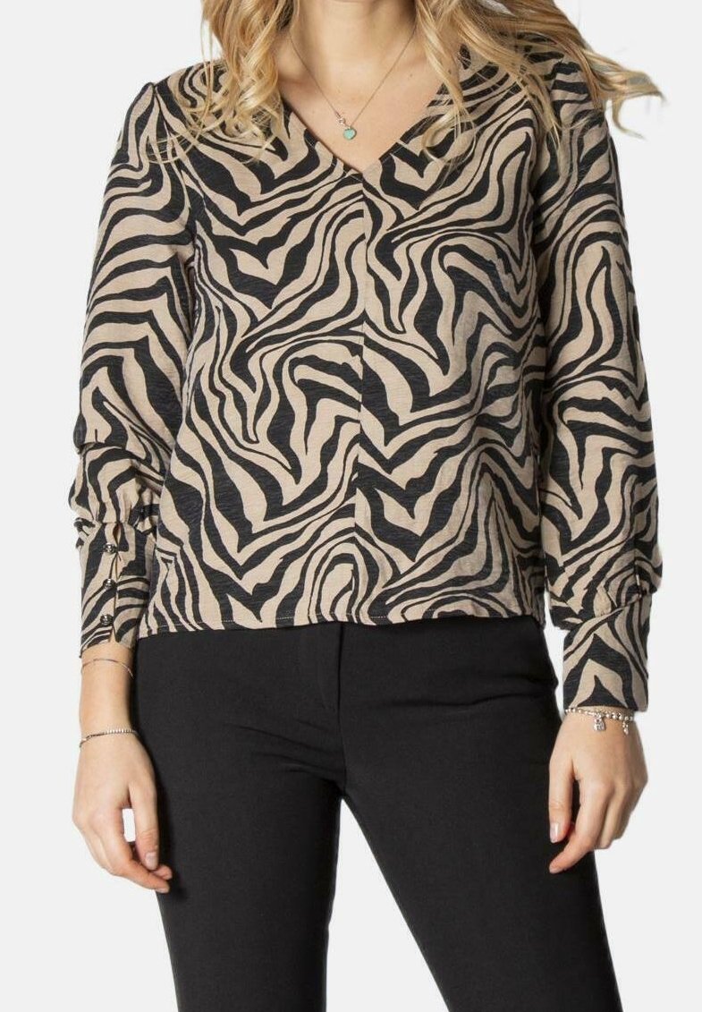 Femme portant un chemisier beige et noir à manches longues avec imprimé zèbre et col en V, ainsi qu’un pantalon noir, montrée du cou aux hanches.