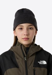 Dark gray knit beanie with a ribbed texture, worn by a person in a brown and black jacket featuring a logo on the chest and a zip closure.