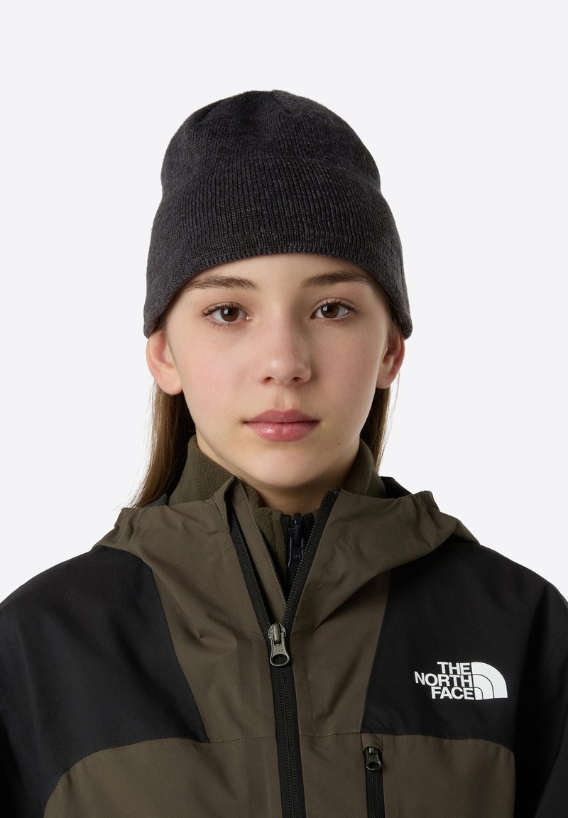 Dark gray knit beanie with a ribbed texture, worn by a person in a brown and black jacket featuring a logo on the chest and a zip closure.