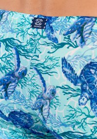 Blaue gemusterte Strandbekleidung mit Meeresschildkröten und marinen Pflanzen auf einem hellen Aqua-Hintergrund, aus dehnbarem Stoff gefertigt.