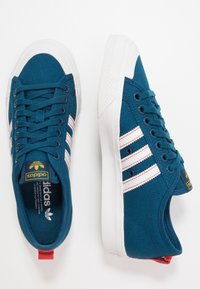 Pár tyrkysových plátěných tenisek Adidas s bílými podrážkami a třemi bílými pruhy, zobrazených z horního a bočního pohledu na bílém pozadí.