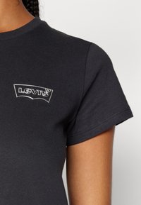 T-shirt en coton noir avec un patch en argent du logo Levi's sur la poitrine gauche. Manches courtes, coupe classique, texture lisse.