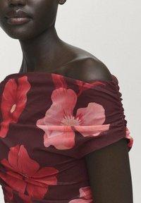Un haut bordeaux à épaules dénudées avec des motifs floraux roses, une texture froncée le long de l'encolure et une coupe ajustée qui épouse le corps.