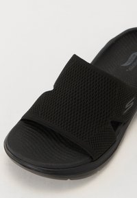 Sorte skyvesandaler med et teksturert mesh-overdel og polstret såle. Har en bred stropp for støtte og et stilrent, minimalistisk design.
