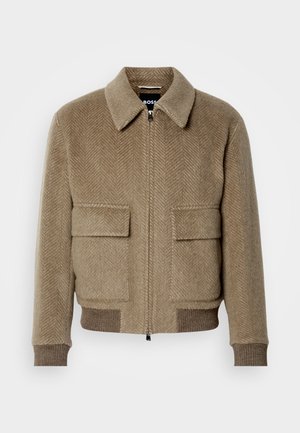Brun herringbone ull bomberjacka med dragkedja fram, två fickor med lock och ribbade ärmslut. Har en klassisk krage och subtil textur.