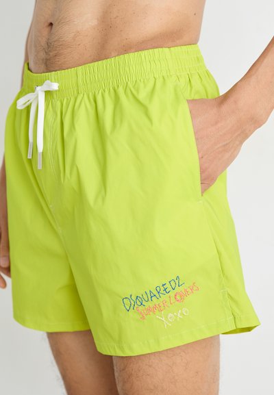 Bañador verde lima con cinturilla elástica, cordón blanco y texto bordado en el lado inferior con letras de colores.