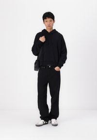 Hoodie preto cropped com cordões, combinado com jeans pretos largos e ténis brancos com detalhes em preto e cinza. Design minimalista.