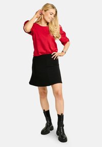 Bluza roșie cu mâneci scurte bufante, asortată cu o fustă neagră până la genunchi. Ghete negre masive până la gleznă, cu panouri elastice pe lateral. Textură netedă.