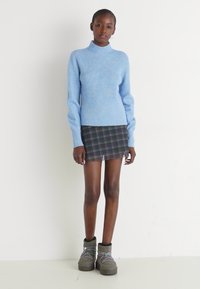 Svetlo modra turtleneck jopica iz mehkega materiala, v kombinaciji s črno karirasto mini krilo in sivo kratko čevljo z vezalkami.