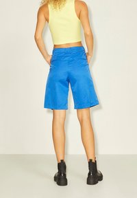 Blå shorts med en slät textur, med mid-rise midja och rak skärning. Bakfickor och en ren finish på sömmarna. Svarta ankelstövlar synliga.