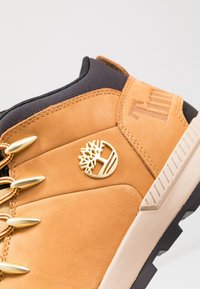 Botte Timberland couleur camel avec col rembourré noir, logo arbre doré, œillets métalliques dorés et semelle beige avec semelle extérieure noire.