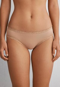 Beige slipjes met kantafwerking, gemaakt van een gladde stof met een zachte textuur. De tailleband heeft een delicate golvende kanteleding.
