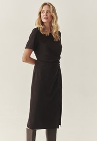 Vestido negro de longitud a la rodilla con mangas cortas, con una apertura lateral y un diseño fruncido en la cintura. Tejido suave y silueta estilizada.
