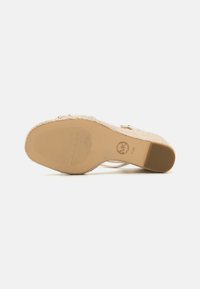 Wedge sandal with a woven jute upper, beige color, and textured rubber sole. Features a metallic ankle strap and a round logo detail.