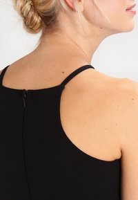 Black dress with thin straps, featuring a concealed back zipper. Smooth texture with a fitted silhouette. Minimalistic design.