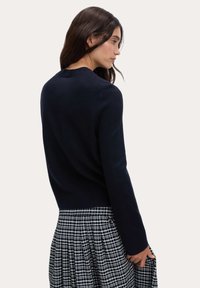 Granatowy sweter dzianinowy z długimi rękawami i ściągaczem, zestawiony z czarno-białą spódnicą w kratkę. Gładka tekstura, okrągły dekolt.