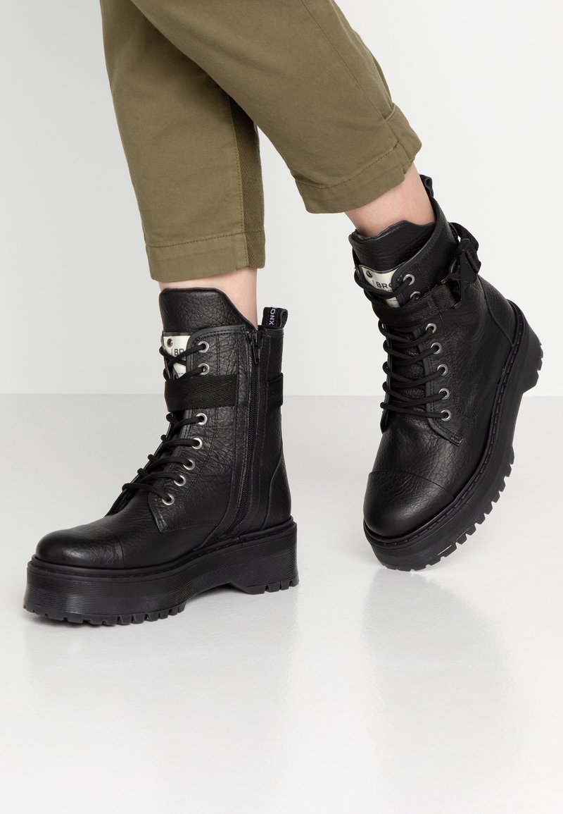 Stivaletti neri in pelle con finitura texturizzata, con chiusura a lacci e zip, dotati di suola in gomma spessa e dettaglio con cinturino alla caviglia.