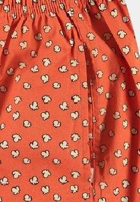 Tissu orange avec un motif de maïs soufflé en crème et noir. Dispose d'une taille élastique et d'une texture lisse. Parfait pour un look décontracté.