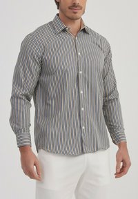 Chemise rayée à manches longues en tissu beige, bleu et blanc. Boutons sur le devant, design ajusté, avec des poignets à boutons et un col classique.