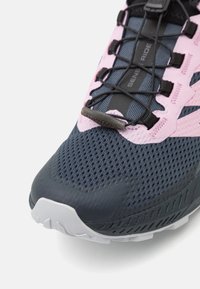 Harmaa ja vaaleanpunainen urheilujalkine, jossa on hengittävä verkkopäällinen, kuvioitu kumipohja ja joustavat nauhat. Varustettu vahvistetulla varvassuojalla ja logoyksityiskohdalla.