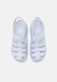Baltas plastmasas sandales ar closed-toe dizainu, ar platām siksnām un aizmugures papēža siksnu drošai pieguļošanai. Tekstūrēta zolīte komfortam.